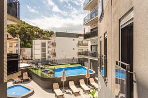 Un área de piscina en la azotea con sillones de descanso, una piscina pequeña y vistas de edificios circundantes.