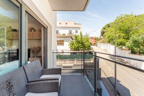A balcony with wicker furniture, a glass door, and a view of buildings and greenery. - Apartment 'Claret' with Mountain Views, Wi-Fi, and Air Conditioning (Lloret de Mar)