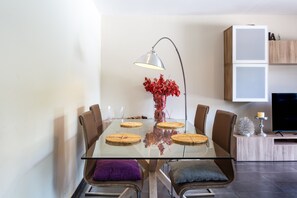 Ein moderner Essbereich mit einem Glastisch, Ledersesseln, einer Vase mit roten Blumen, einer Stehlampe und einem Fernseher auf einem Holzschrank.