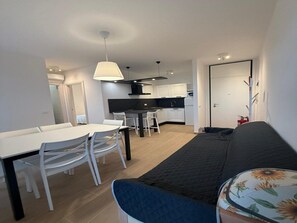A compact living space with a dining area, kitchenette, and a sofa. - Sea View Escape at Lido dei Pini (San Michele al Tagliamento)