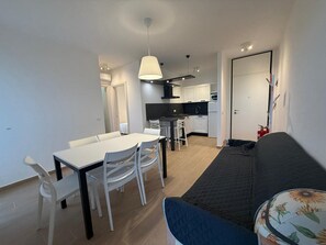 A modern apartment with a dining area, kitchenette, and a living room with a sofa. - Sea View Escape at Lido dei Pini (San Michele al Tagliamento)