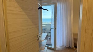A room with a wooden door, a view of the beach, a small table, and a chair. - Sea View Escape at Lido dei Pini (San Michele al Tagliamento)