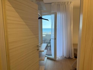 Ein Zimmer mit Holztür, Blick auf den Strand, einem kleinen Tisch und einem Stuhl.