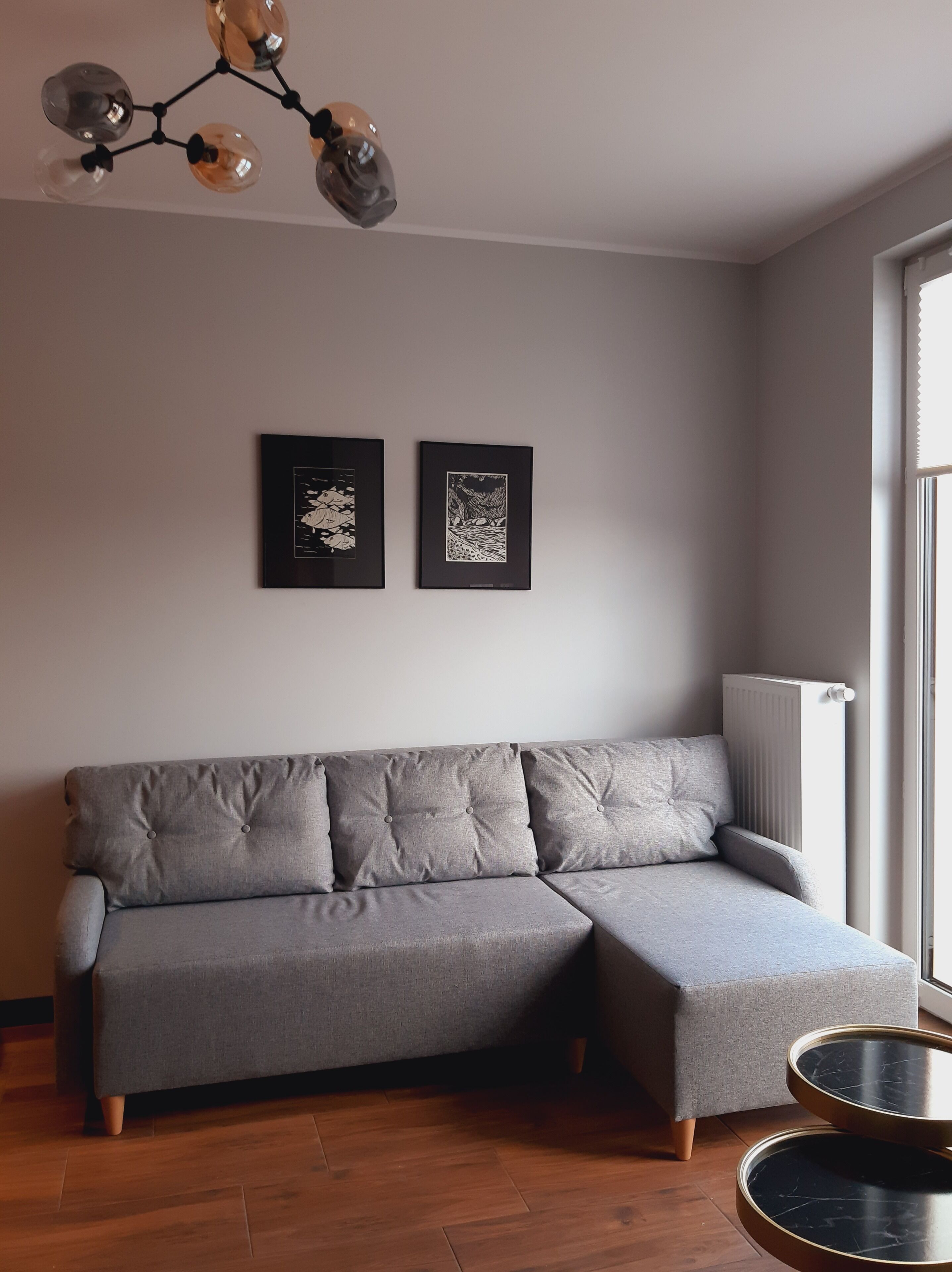 A grey sectional sofa, two framed artworks, a modern chandelier, and a radiator.