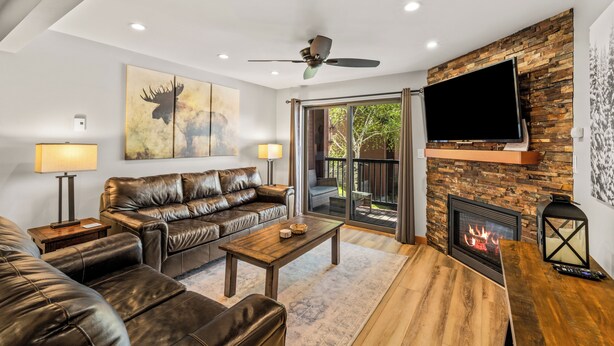 A living room with a leather sofa, a coffee table, a fireplace, and a television mounted on a stone wall. - Steps to the Gondola~Pool, Hot Tubs~In-Unit Laundry (Steamboat Springs)