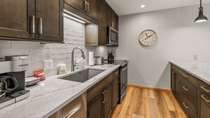 A modern kitchen with dark wood cabinets, a stainless steel microwave, a coffee maker, and a clock on the wall. - Steps to the Gondola~Pool, Hot Tubs~In-Unit Laundry (Steamboat Springs)