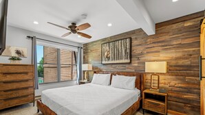 A bedroom with a large bed, wooden wall paneling, a ceiling fan, and a window with a view. - Steps to the Gondola~Pool, Hot Tubs~In-Unit Laundry (Steamboat Springs)