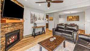 A living room with a fireplace, leather sofa, wooden coffee table, and a ceiling fan. - Steps to the Gondola~Pool, Hot Tubs~In-Unit Laundry (Steamboat Springs)