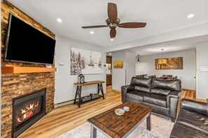 Ein Wohnzimmer mit Kamin, Ledersofa, Couchtisch aus Holz und Deckenventilator.