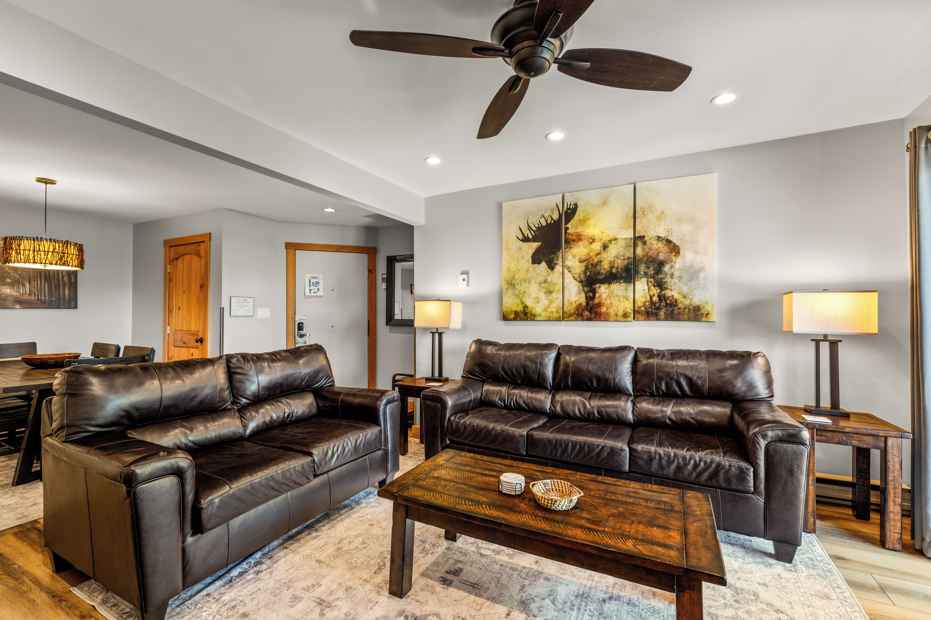 A modern living room with two leather sofas, a wooden coffee table, and a ceiling fan.
