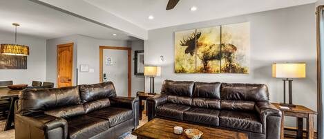 A modern living room with two leather sofas, a wooden coffee table, and a ceiling fan.