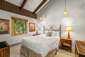 A bedroom with a large bed, two bedside tables with lamps, a window with a view of trees, and a wooden headboard. - Slope Day Hideaway | Fireplace & Winter Shuttle (Steamboat Springs)