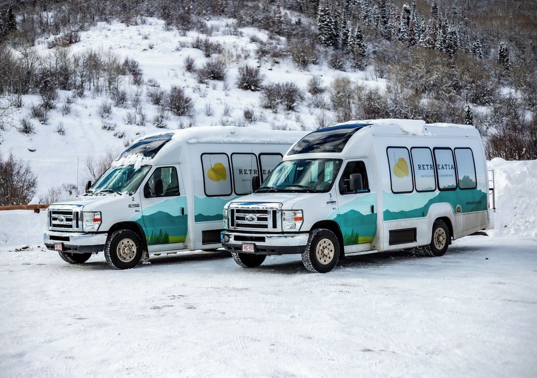 Two white recreational vehicles parked on a snowy surface with a mountainous background.