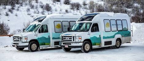 Two white recreational vehicles parked on a snowy surface with a mountainous background.