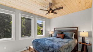 Un dormitorio con una cama grande, techo de madera y ventanas que dan a árboles.