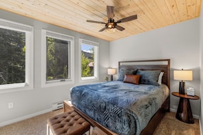 Ein Schlafzimmer mit einem großen Bett, Holzboden und Fenstern mit Blick auf Bäume.
