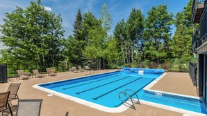 Una piscina rectangular con revestimiento azul, rodeada de sillas de descanso y una solana de hormigón.