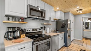 Una cocina moderna con electrodomésticos de acero inoxidable, armarios blancos y techo de madera.
