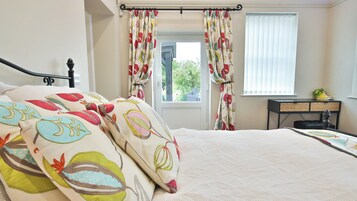 Un dormitorio con cama, cortinas, una ventana y un escritorio con una planta.