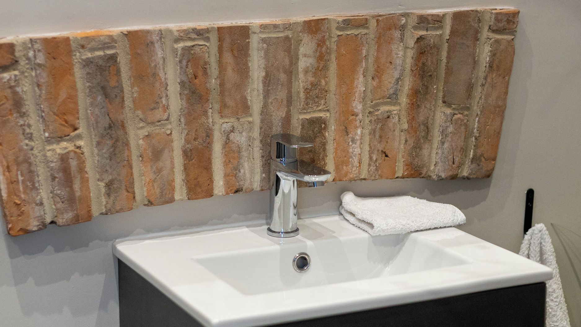 Un bany amb un lavabo blanc, un aixeta modern i una paret amb relleu a la part superior.