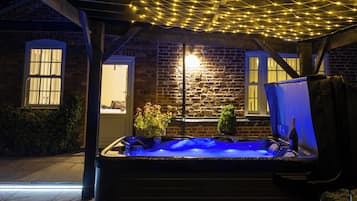 Un jacuzzi con luz azul, rodeado por un muro de ladrillo y vigas de madera, con luces colgantes en el techo.