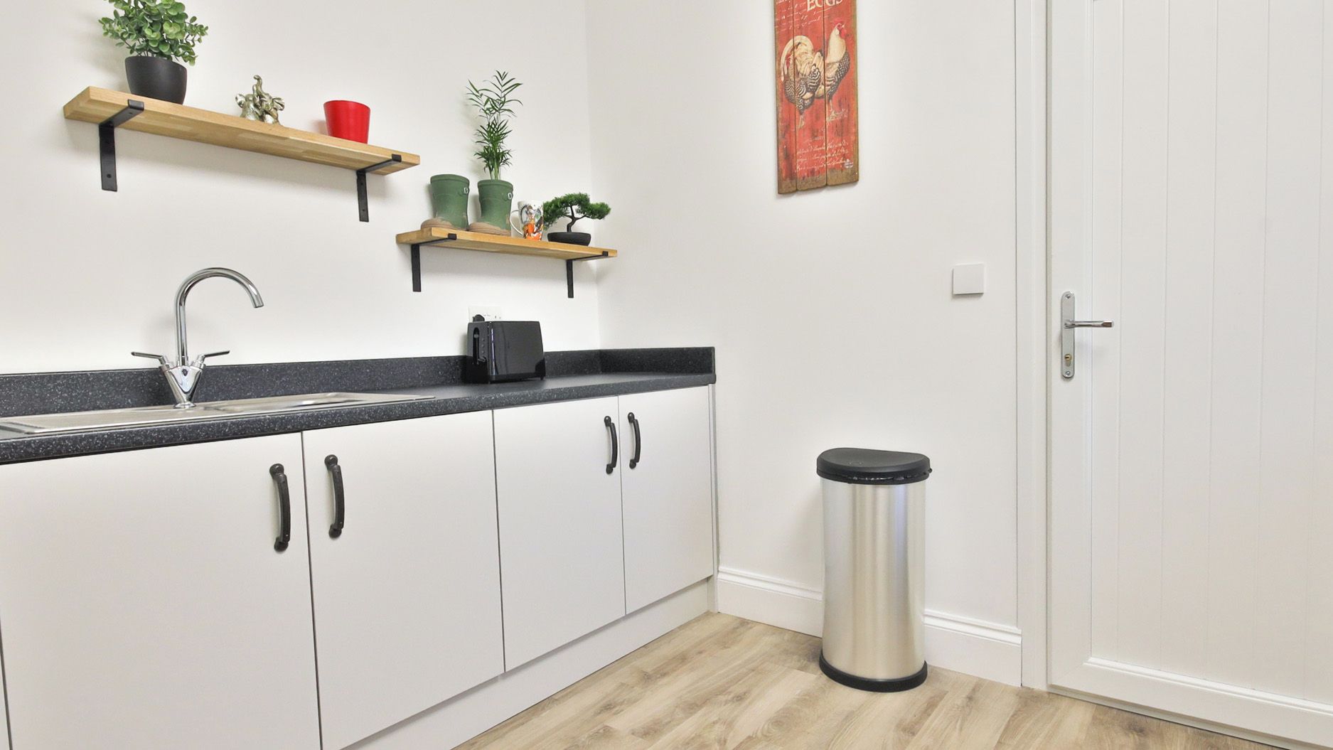 A kitchen with white cabinets, a black countertop, a stainless steel trash can, and a door.