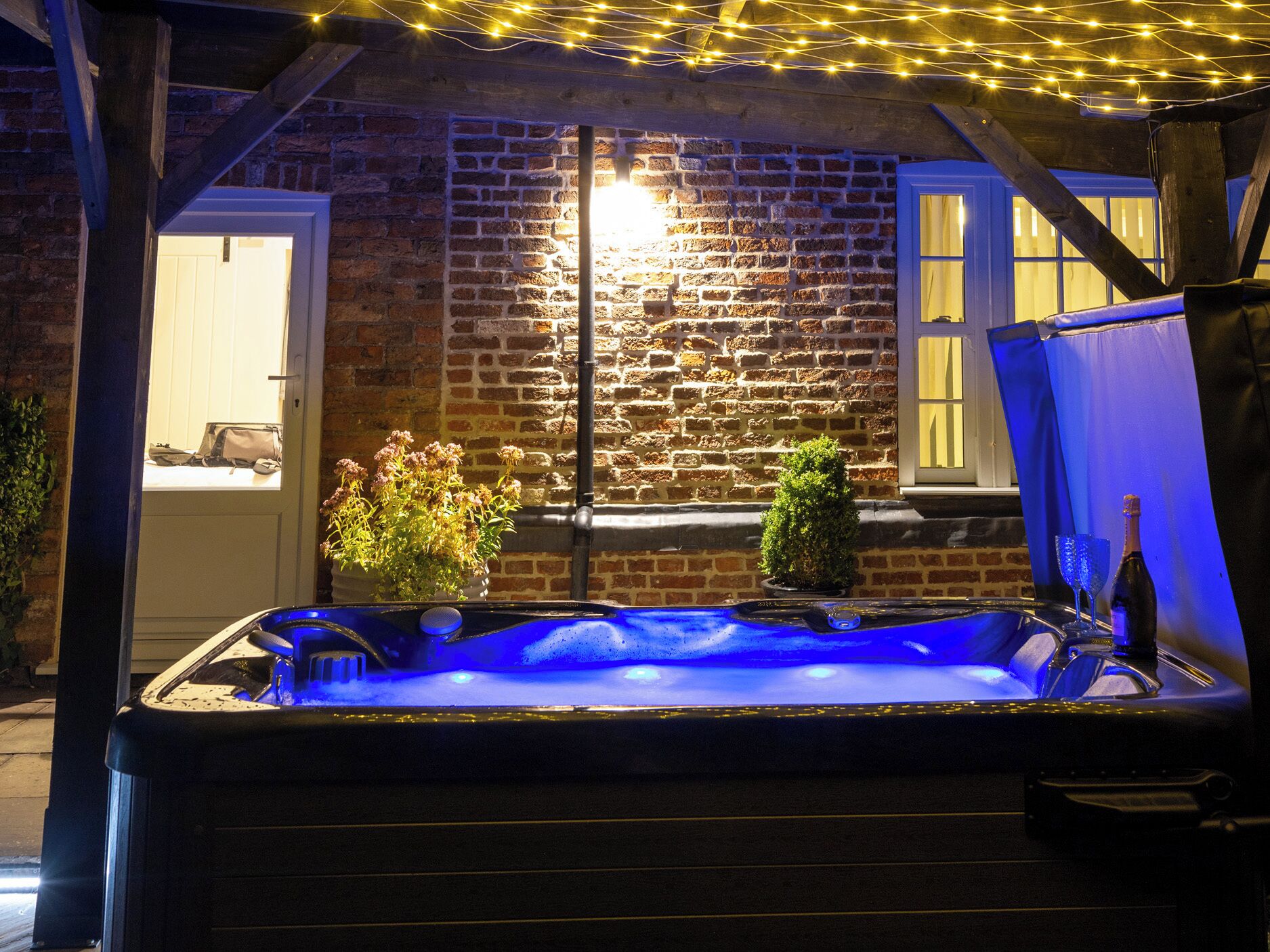 Un jacuzzi iluminado con luz azul, rodeado por un muro de ladrillo y una estructura de madera.