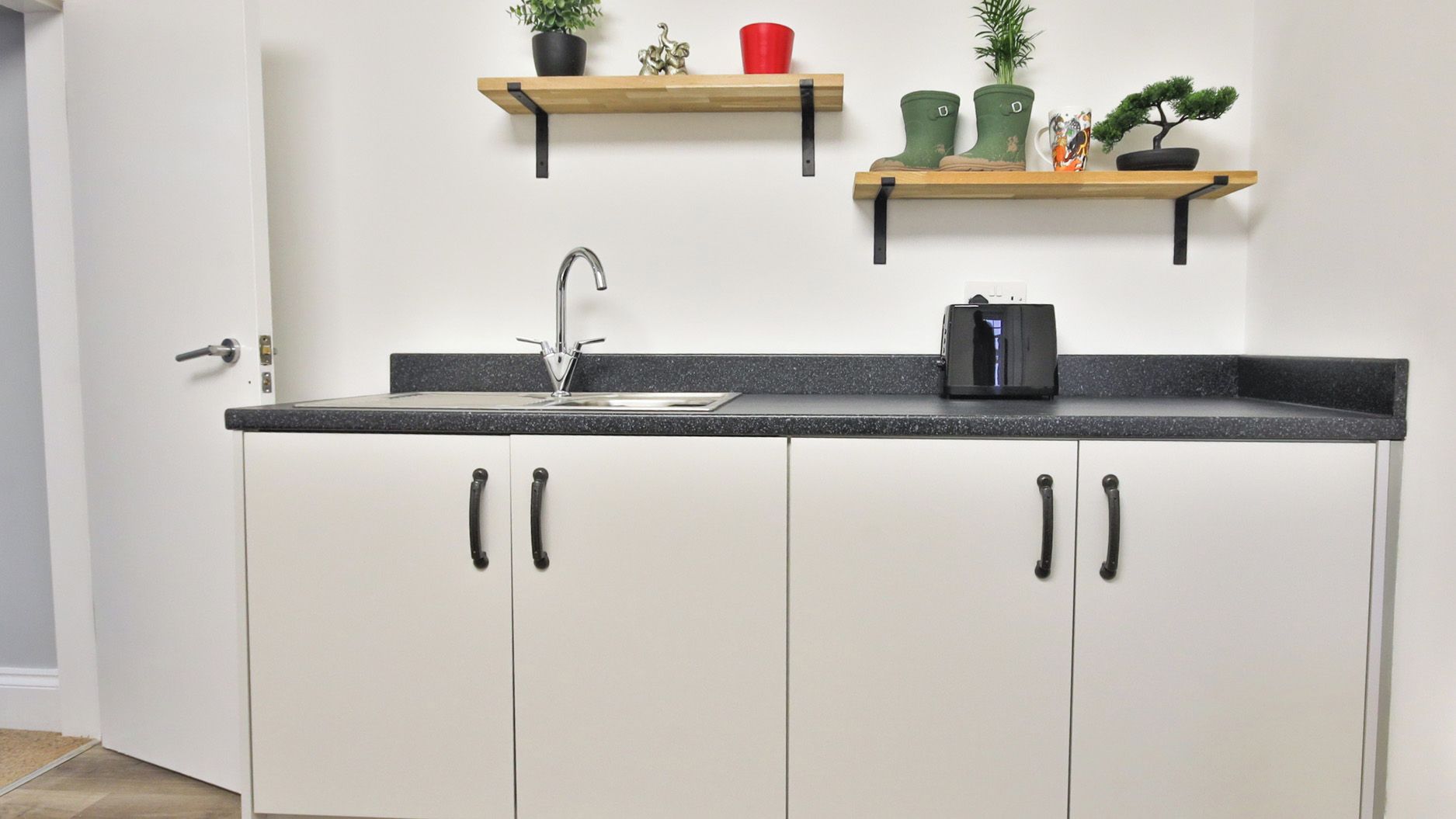 Cocina con pileta, alacenas y dos estantes superiores con objetos decorativos.