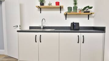 Cocina con pileta, alacenas y dos estantes superiores con objetos decorativos.