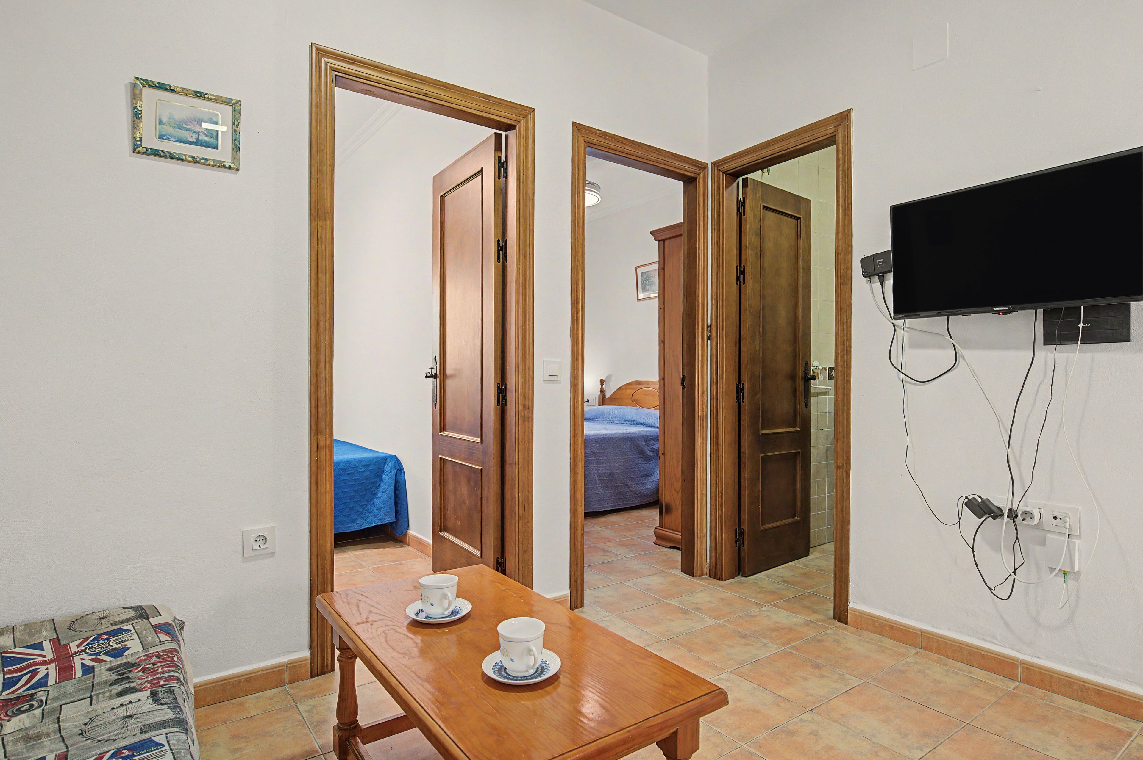 Een hotelkamer met een houten tafel, twee bekers, een bed met een blauwe spreidek en een televisie aan de muur.