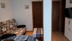 A small room with a sofa, a table, a door, and a TV mounted on the wall. - Casa Olivo – Conil de la Frontera, 2 bedrooms, apartment, 4 guests (Conil de la Frontera)