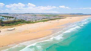 A coastal beach with a sandy shore, a clear blue sky, and distant hills. - Casa Olivo – Conil de la Frontera, 2 bedrooms, apartment, 4 guests (Conil de la Frontera)