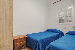 Ein schlichter Raum mit zwei Einzelbetten, einem Holz-Nachttisch und einem Fenster mit Ausblick.