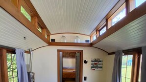 A compact room with a bunk bed, a small table, and a sofa with floral bedding. - Beautiful custom tiny home 20 min from Middlebury! (Addison)