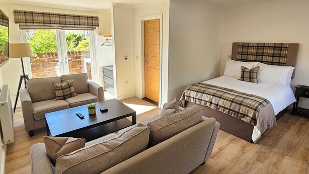 A modern hotel room with a bed, sofa, coffee table, and a view of the outdoors.