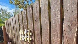 A wooden fence with two hanging decorations: a wooden cross and a jar with flowers.