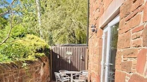 A stone patio with a table and chairs, a wooden fence, and a brick wall.