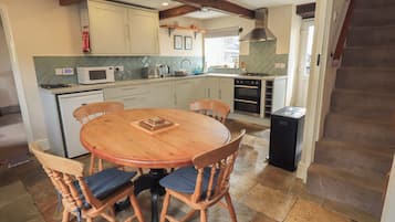 Une cuisine avec une table ronde en bois et des chaises, un four à micro-ondes, une cuisinière et des placards.