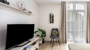 A modern living room with a flat-screen TV, a plant, a chair, and a large window with curtains.