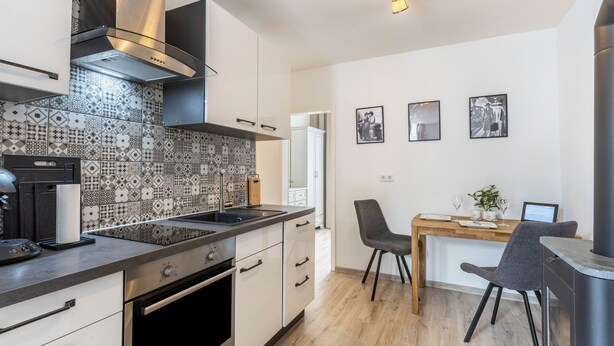 A modern kitchen with a patterned backsplash, stainless steel appliances, and a dining area with a wooden table and chairs.