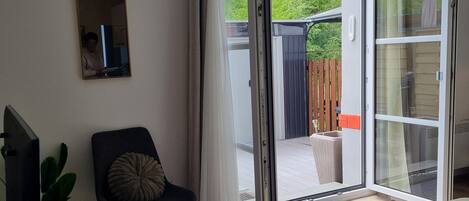 A modern living room with a television, a chair, a sofa, and a sliding glass door leading to an outdoor area.