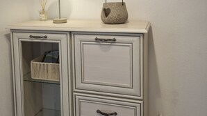 A white cabinet with glass doors and drawers, a framed abstract artwork above it, and a small table with a lamp and decorative items. - 'Meini' Holiday Apartment in the Old Train Station (Brilon)