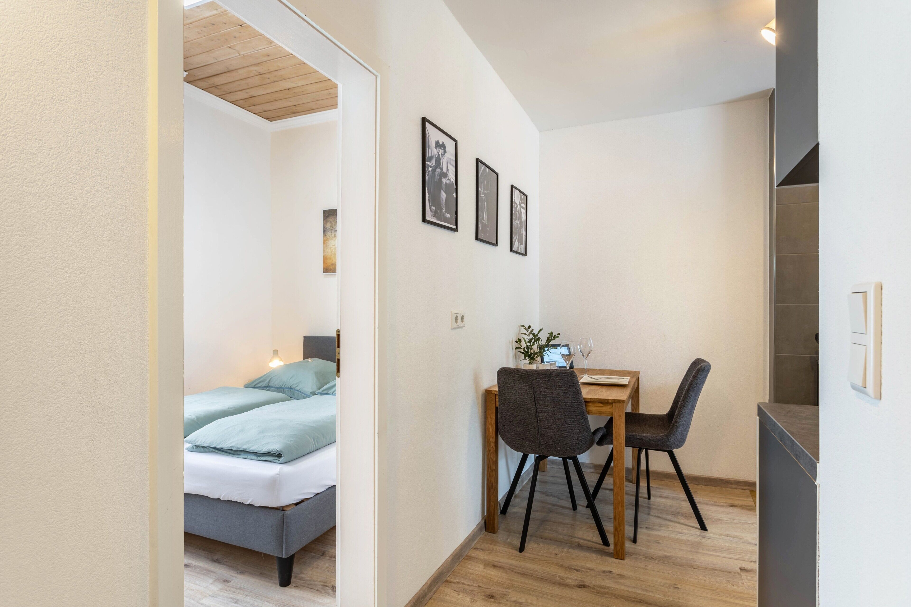 Een compacte kamer met een bed, een eettafel met stoelen en een kitchenette.