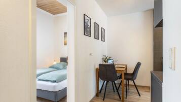 Een compacte kamer met een bed, een eettafel met stoelen en een kitchenette.