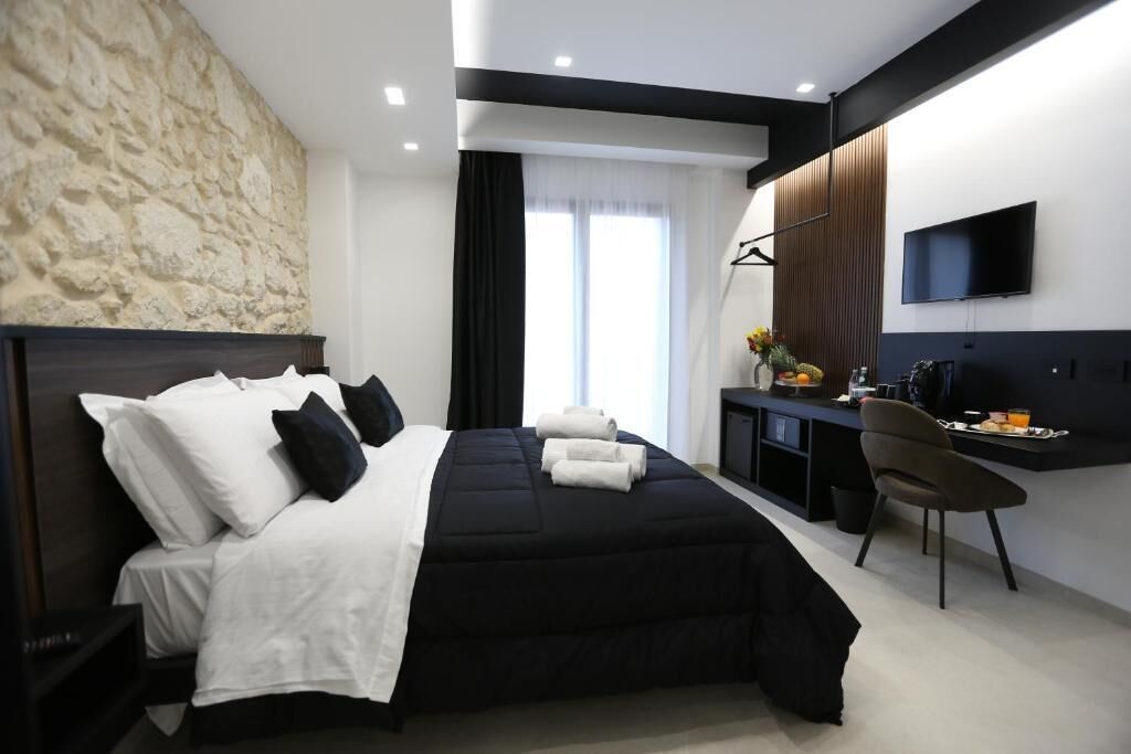 Una habitación de hotel moderna con una pared de acento de piedra, una cama grande con ropa de cama blanca y negra, un escritorio con una silla y un televisor de pantalla plana montado en la pared.