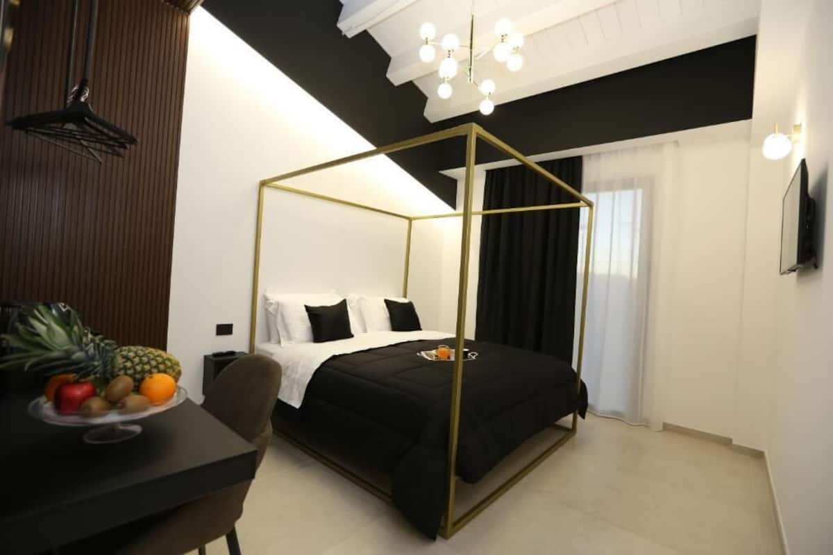 A modern hotel room with a four-poster bed, a dining table with fruit, and a TV on the wall.
