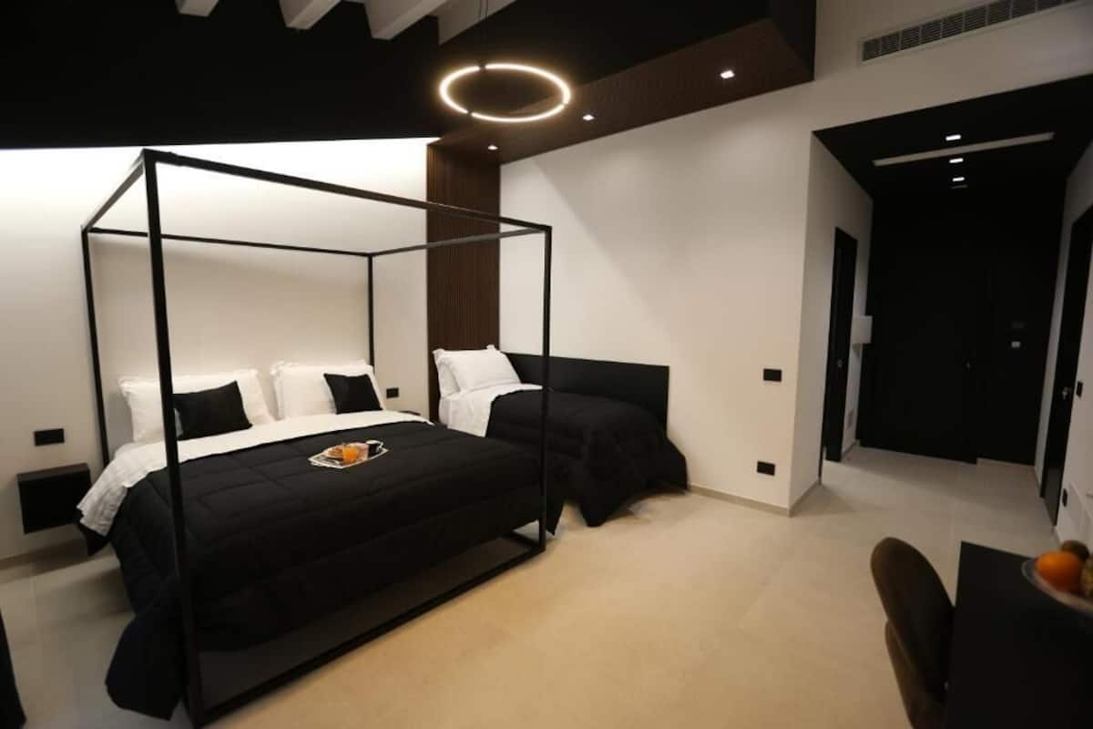 A modern bedroom with a four-poster bed, a small table with fruit, and a chair.