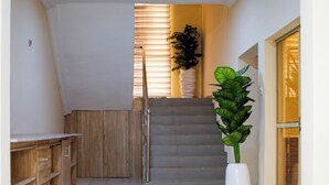 Un pasillo con una escalera, armarios de madera, una planta en maceta y una puerta de cristal.