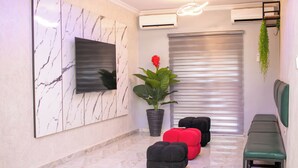 Un interior moderno con una pared de mármol, un televisor montado, una planta en maceta y un banco.