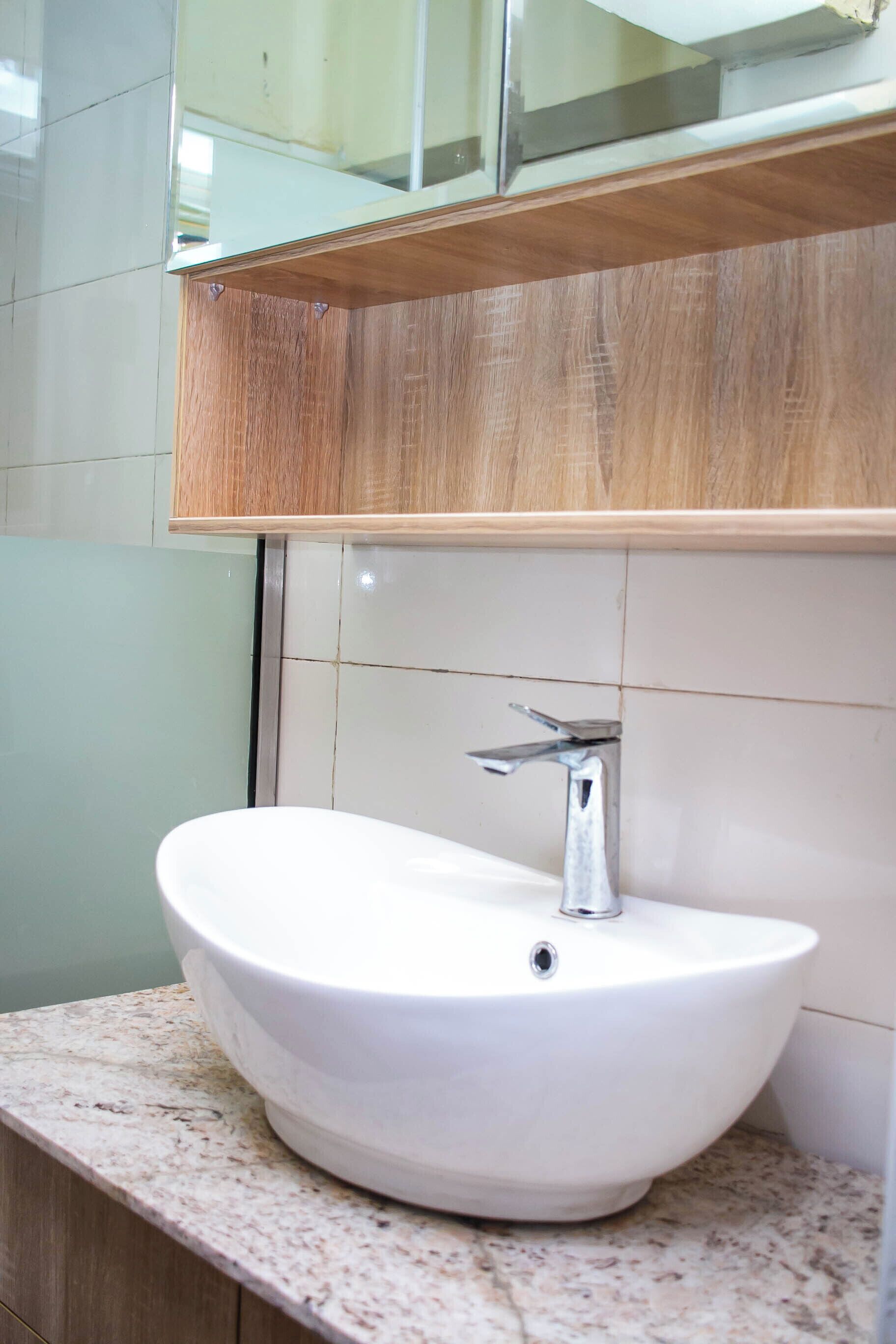 A bathroom with a white vessel sink, a chrome faucet, a wooden vanity, and a mirror above the sink.